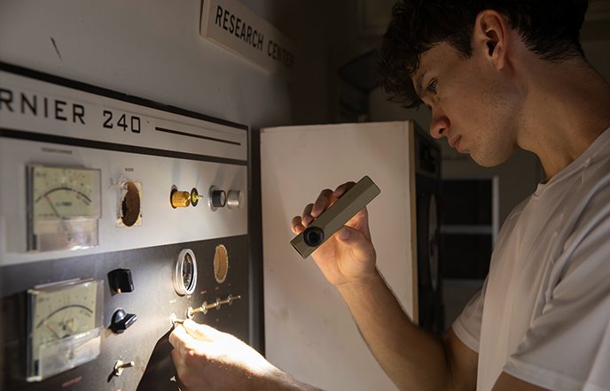 Young researcher inspecting vintage Garnier 240 control panel dials with a flashlight
